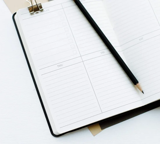 A black pencil lying across an open diary.